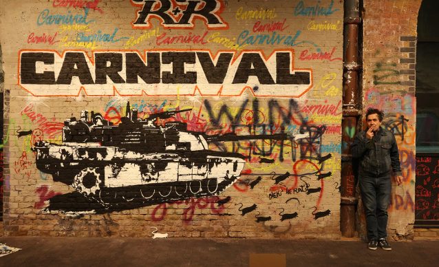 French artist Blek le Rat standing next to a piece of street art in the Leake Street Graffiti Tunnel in London.