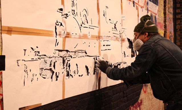 Artist applying a stencil to a large piece of paper in Leake Street Tunnel.